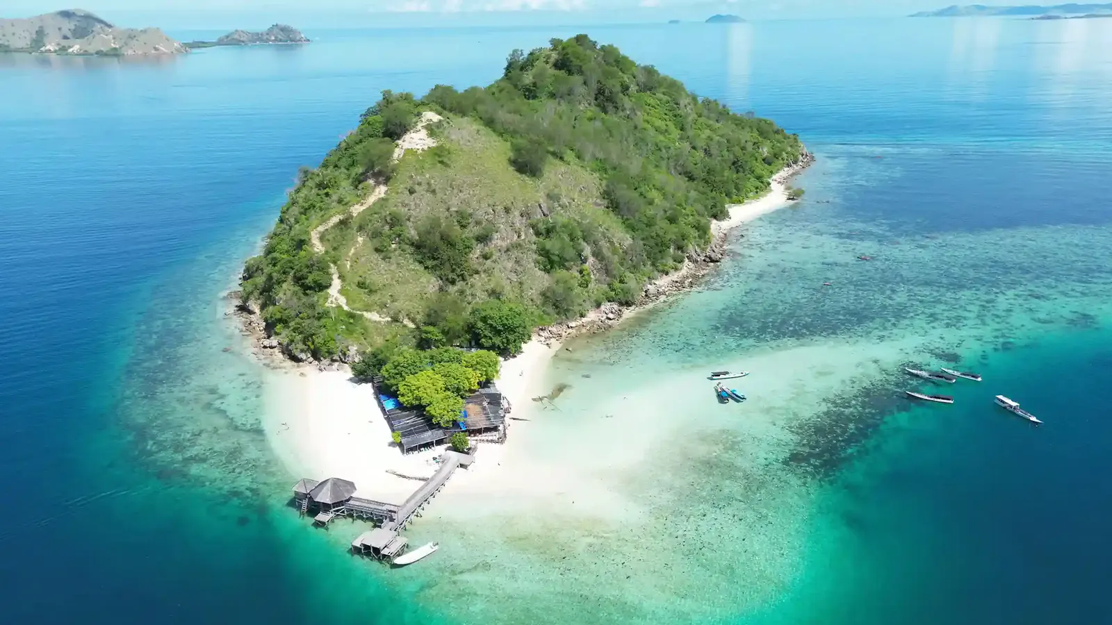 Aerial view of Kelor Island's green hill, white sand spit, jetty and turquoise reef flats
