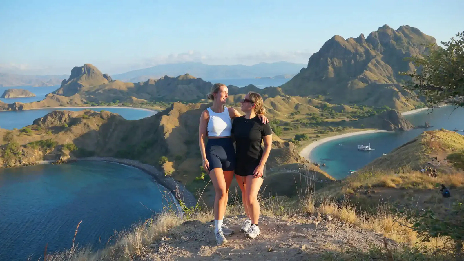 Two hikers posing on the Padar Island ridge above its famous multi-bay coastline