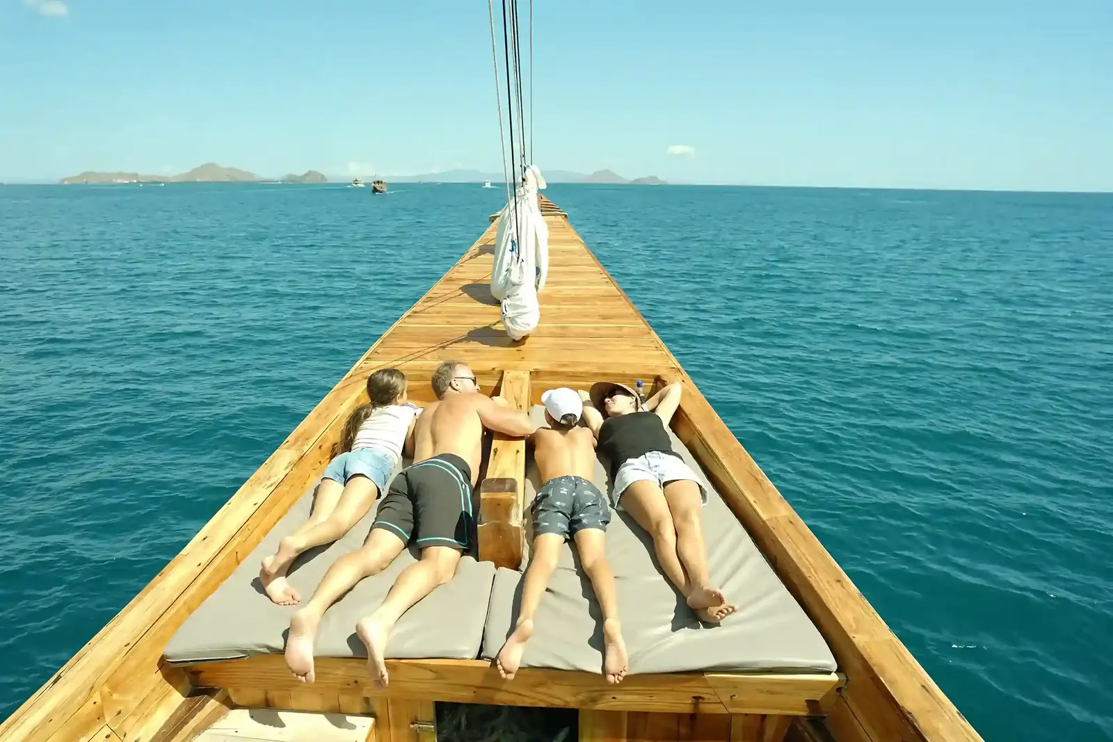 Family of four lying on bow cushions of a wooden boat as it cruises through Komodo waters