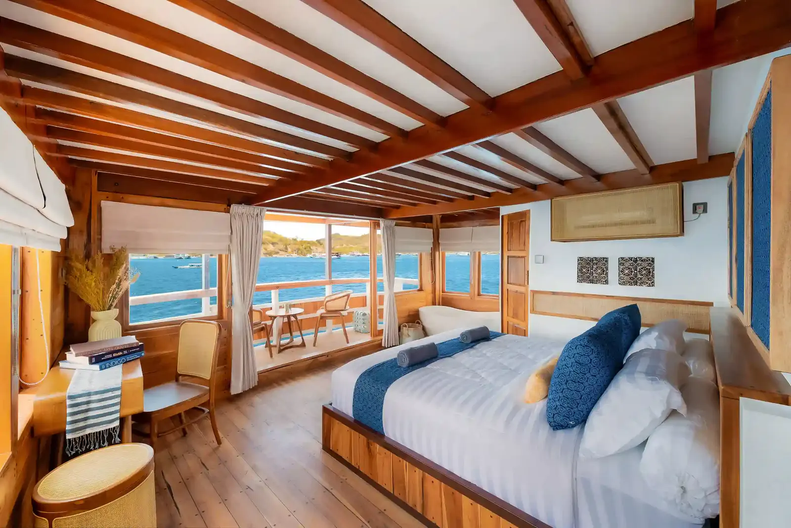 Phinisi master cabin with a double bed, timber-beamed ceiling and sea-view windows to a balcony