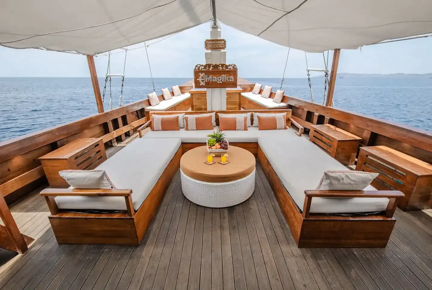 Shaded foredeck lounge of a phinisi with cushioned daybeds and a round table facing the sea