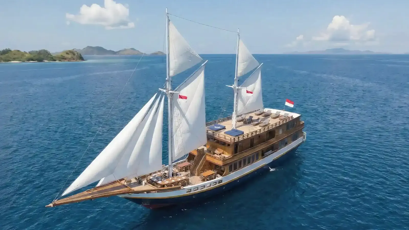 Aerial view of a wooden phinisi under full white sail on deep blue sea among Komodo islands