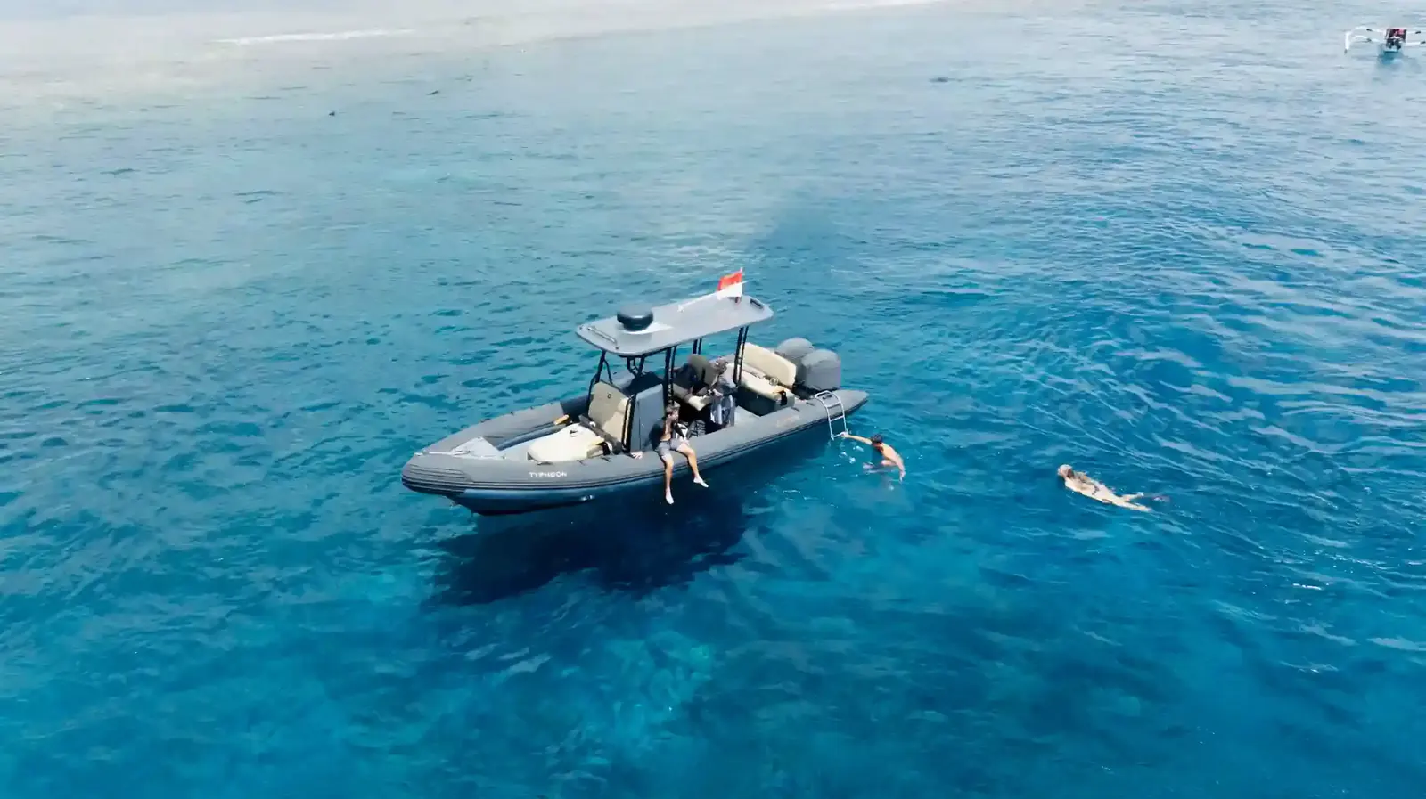 Aerial view of an inflatable tender boat with guests swimming and snorkelling off its side in blue sea