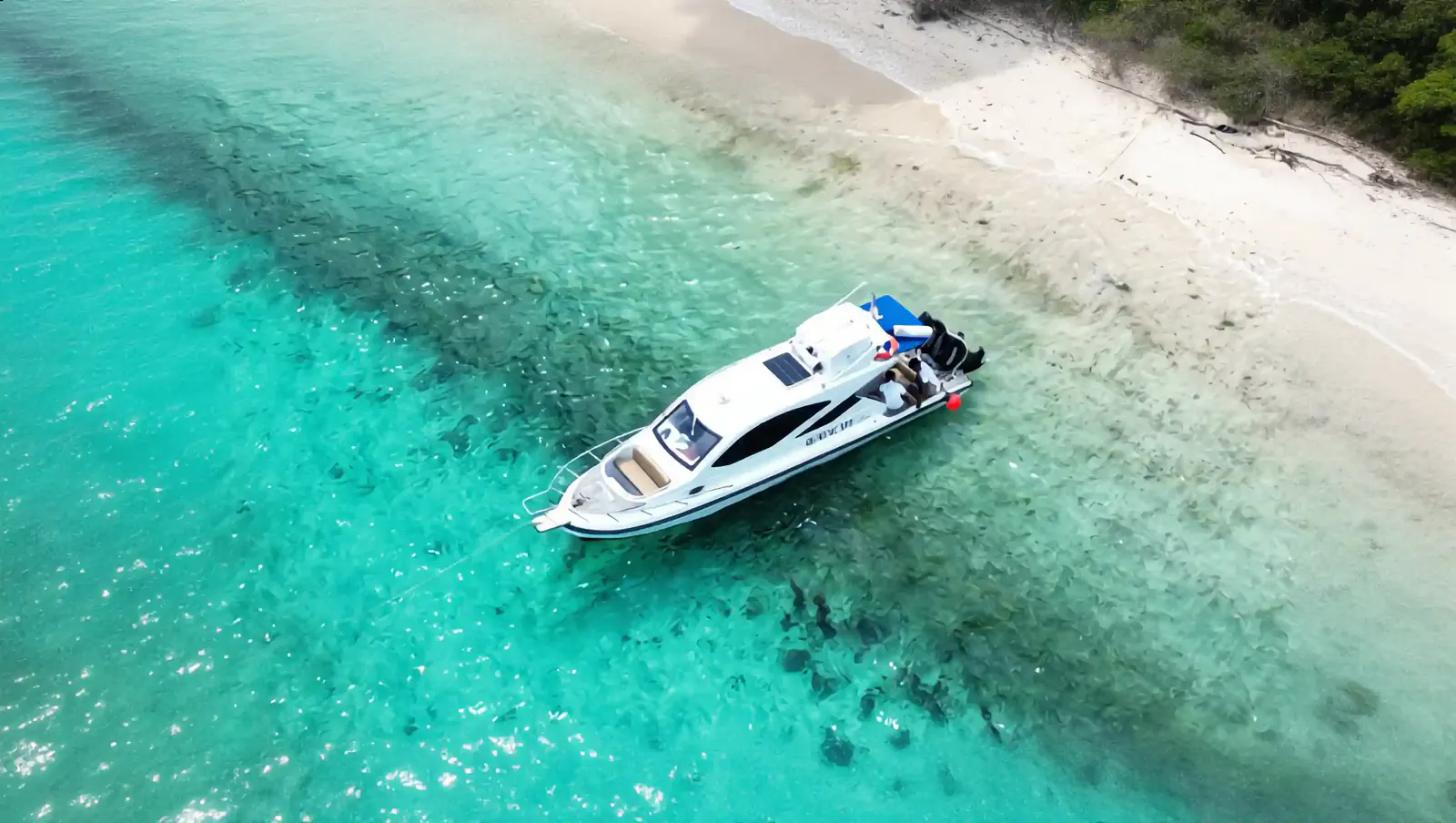 Aerial view of a white speedboat anchored in clear turquoise shallows beside a white-sand beach